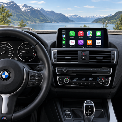 CarPlay-skjerm med appmeny montert over lufteventilene i BMW 1-/2-serie, med fjord og fjell i bakgrunnen.